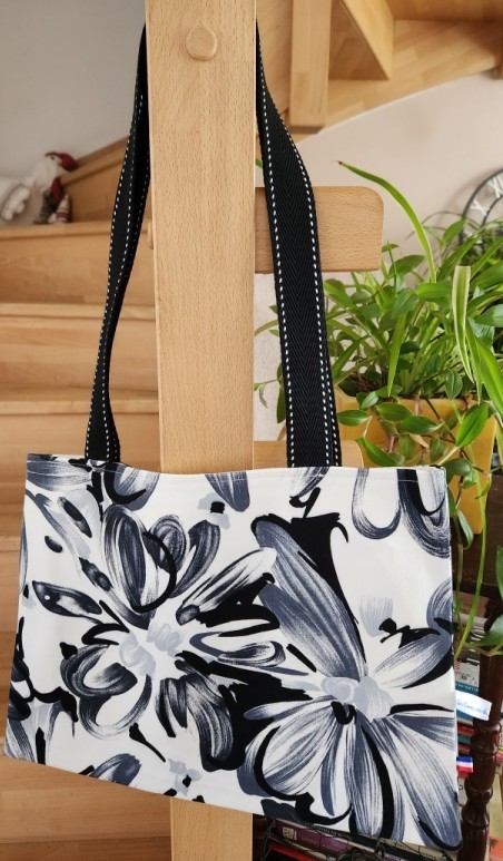 Sac pour petit ordinateur ou tablette noir et blanc à fleurs, dimensions L38 cm x H27,5 cm, avec sangle noire et blanche, 1 poche intérieure, vue côté 1.