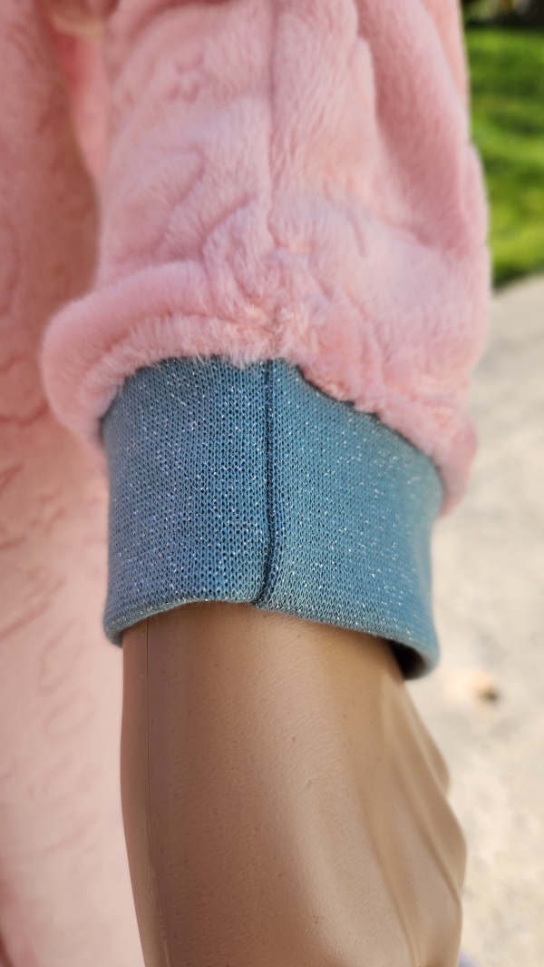 Détail du poignet avec coutures croisées sur une grenouillère adaptée rose, bord côte vert pailleté.