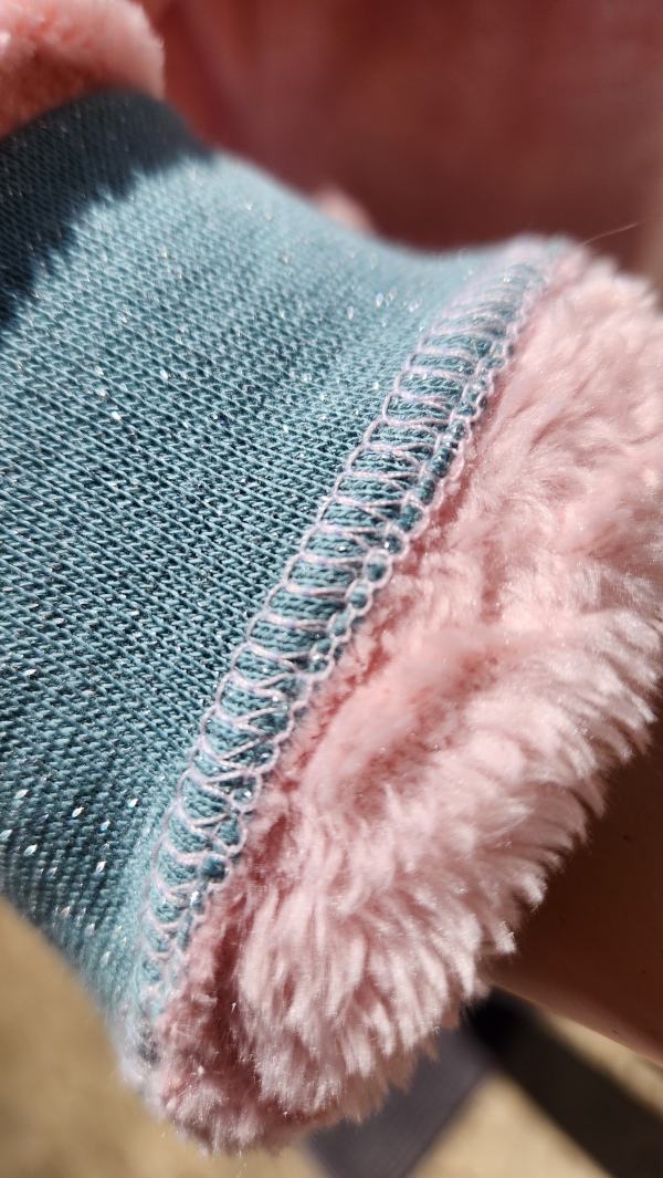 Finition poignet en surjet sur grenouillère adaptée rose avec bords en côte vert pailleté, modèle chaud pour l’hiver.